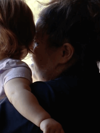 This picture has an adult woman holding a toddler looking outside a window
