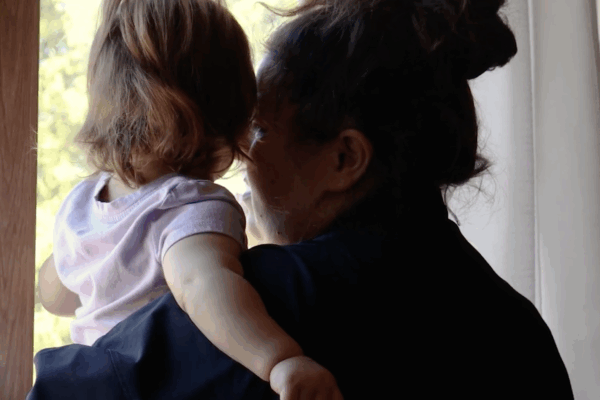 This picture has an adult woman holding a toddler looking outside a window