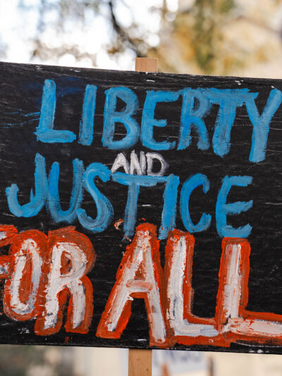 It is a picket sign outside that says in red and blue color Liberty and Justice For All.