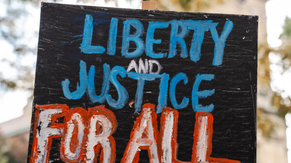 It is a picket sign outside that says in red and blue color Liberty and Justice For All.