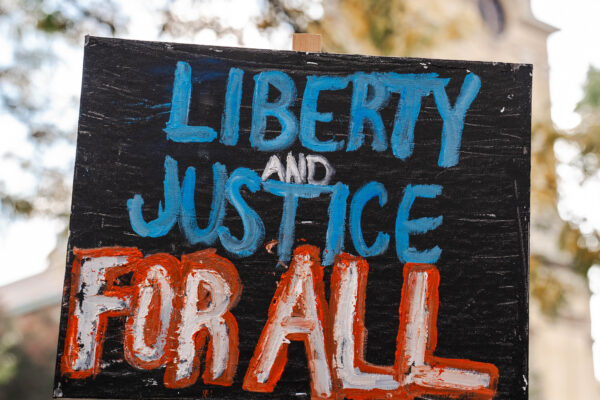 It is a picket sign outside that says in red and blue color Liberty and Justice For All.