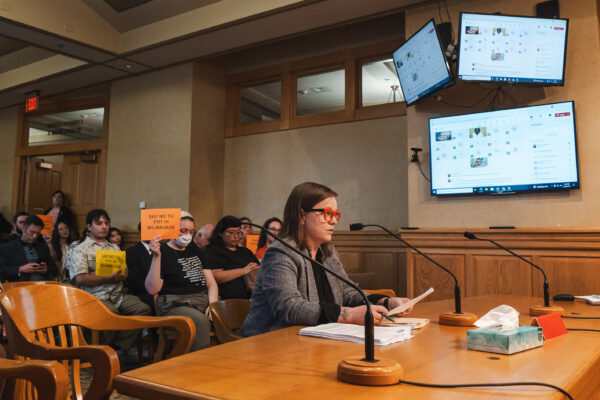 Policy Director Amanda Merkwae testifying in front of the Milwaukee Equal Rights Commission and protesters holding signs reading "No FRT in MKE"