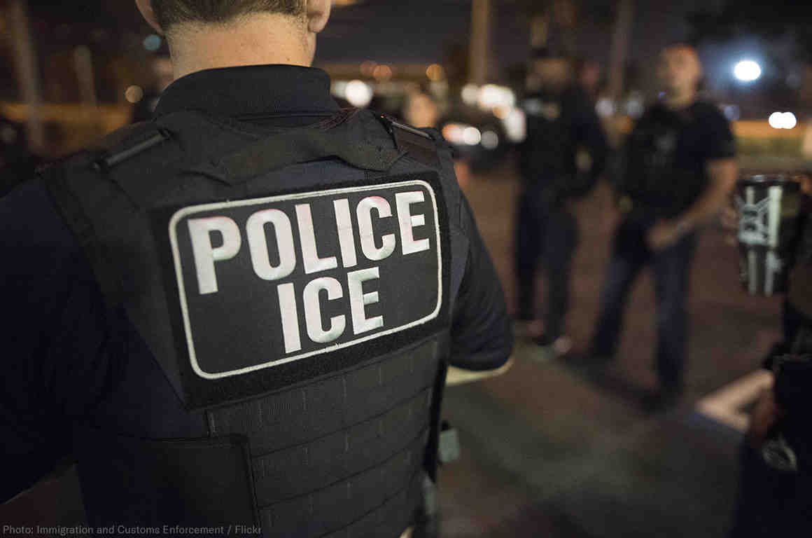 police officer with a flak jacket reading "POLICE ICE"