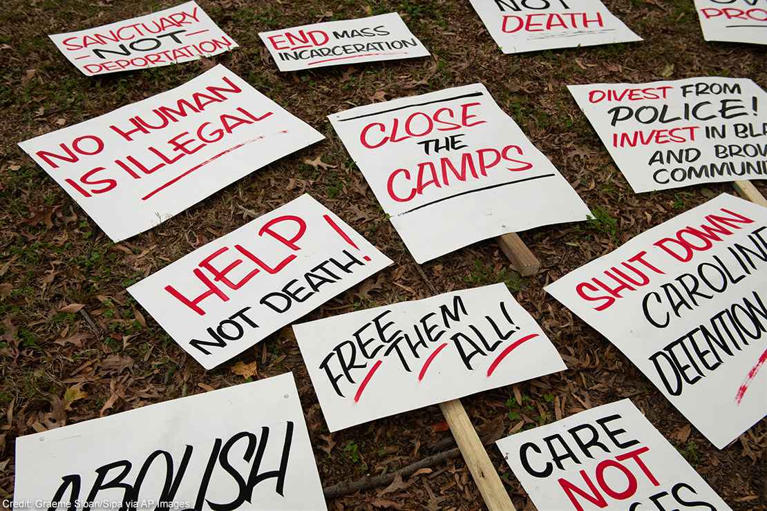 Several signs with calls to end mass incarceration and advocate for the rights of immigrants lying in the grass.