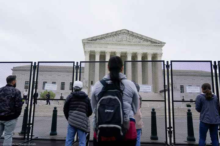 Standing beyond security gates that have signs reading "Area Closed", several people stare at the Supreme Court building.