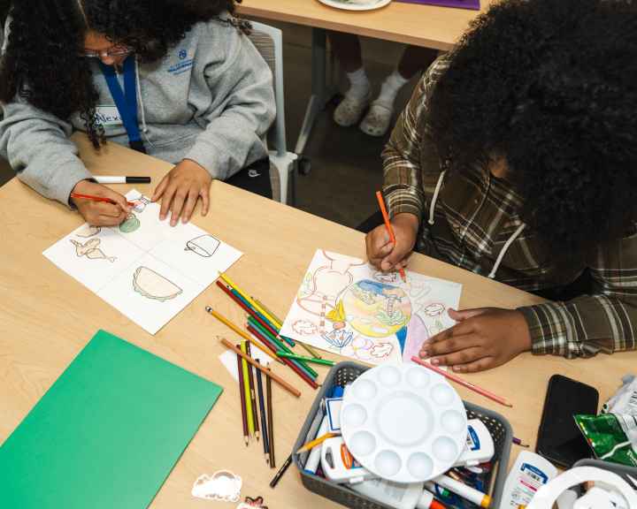 A photo of two studens at a table drawing with art supplies around them