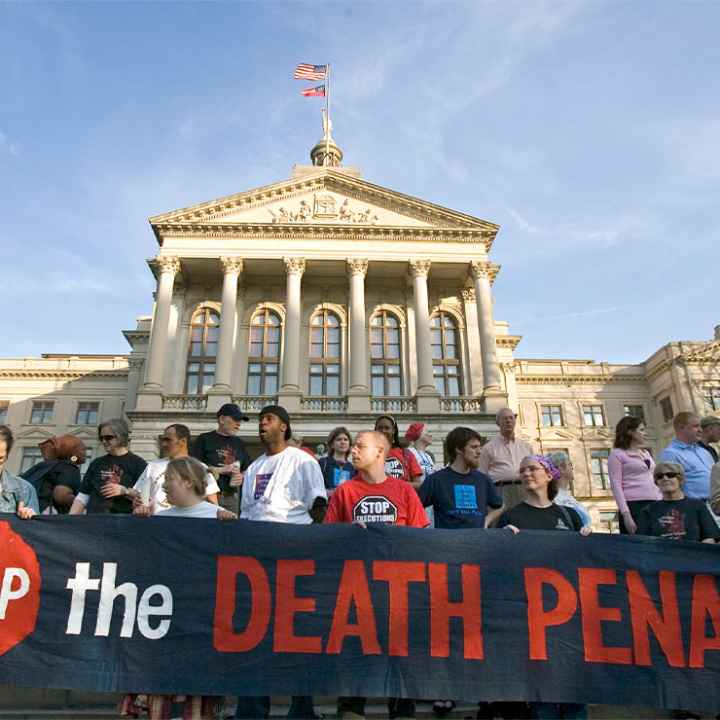 Demonstrators, holding a sign reading "STOP THE DEATH PENALTY", stand on the steps of the State Capitol in Atlanta.