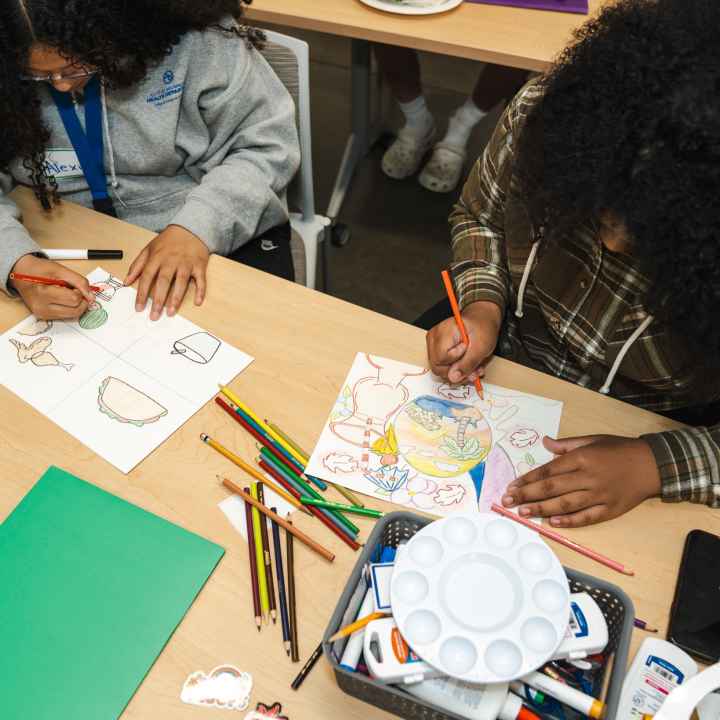 A photo of two studens at a table drawing with art supplies around them