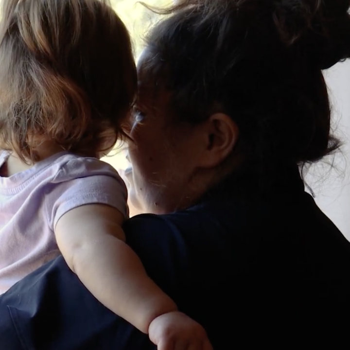 This picture has an adult woman holding a toddler looking outside a window